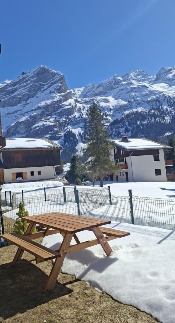 A wooden picnic table in a snowy outdoor area with a mountain backdrop.
