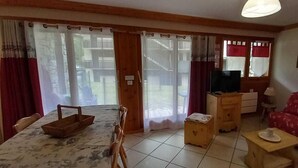 A living room with a sofa, a table, a TV, and a window with curtains.