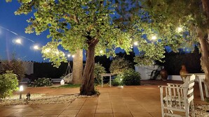 An outdoor patio area with a large tree, string lights, and a white bench. - Villa Angela | Beautiful Villa with Pool in Puglia in Polignano a Mare, Italy (Polignano a Mare)