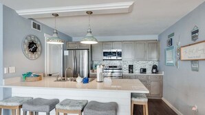 Cocina con una isla central, taburetes de bar, electrodomésticos de acero inoxidable y elementos decorativos en la pared.
