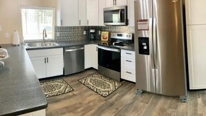 Moderni keittiö, jossa on ruostumattomasta teräksestä valmistetut kodinkoneet, valkoiset kaapit ja kuviolliset matot.