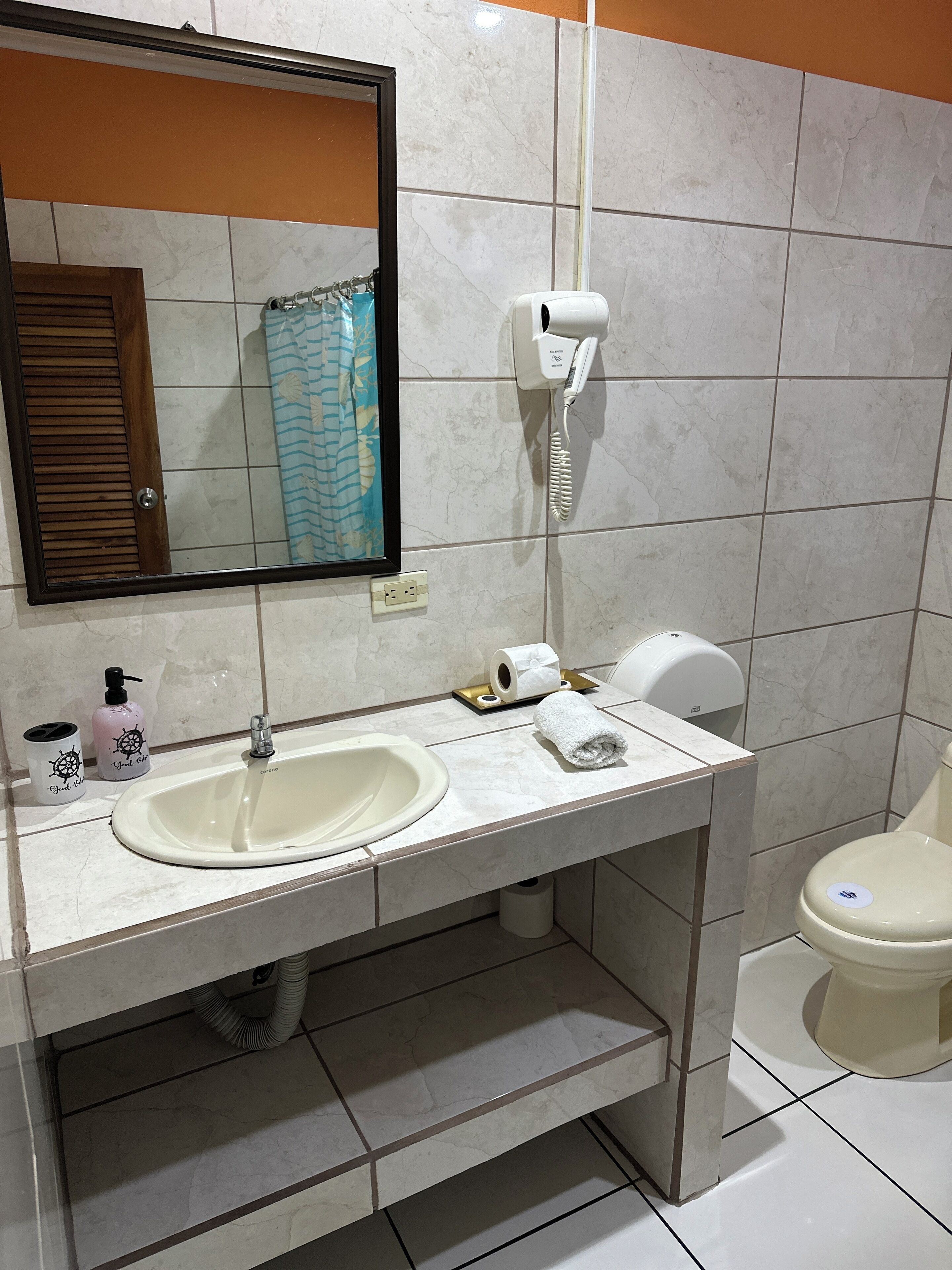 Un baño con lavamanos, espejo, inodoro y secador de pelo en la pared.