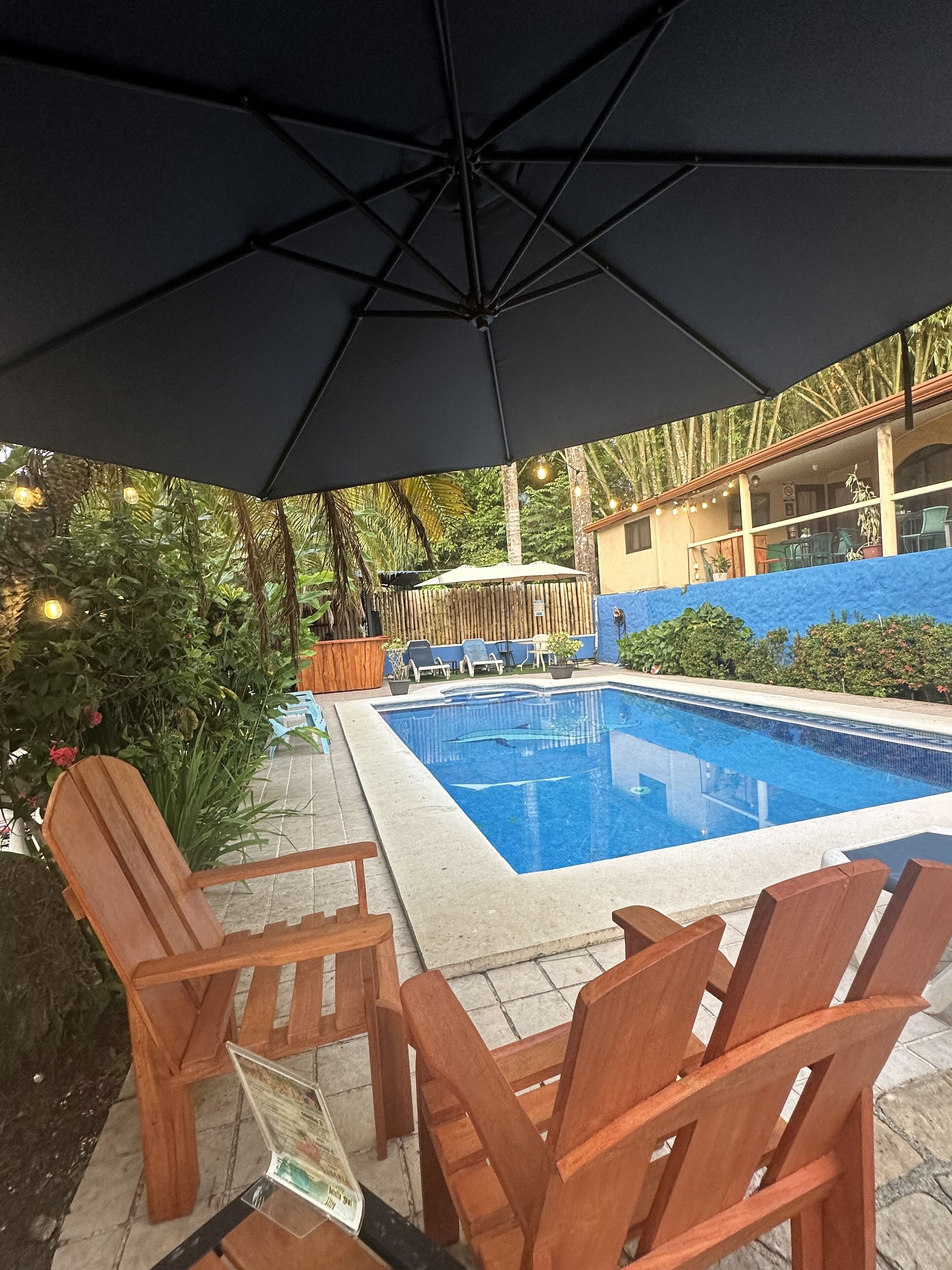 Zona junto a la piscina con sillas de madera, una sombrilla negra y una piscina.