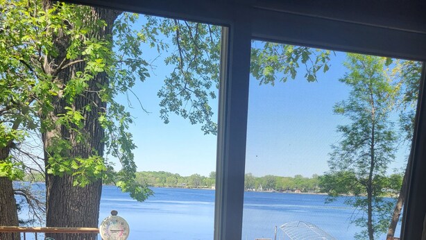 A wooden deck with a view of a lake, a covered seating area, and a weathered wooden bench.