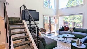 Un vaste espace de vie comprenant un escalier, un ventilateur de plafond et de grandes fenêtres offrant une vue sur l’extérieur.