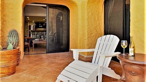 Une chaise blanche et une table sur lesquelles se trouvent une bouteille et un verre, le tout sur une terrasse carrelée, avec un cactus en pot.