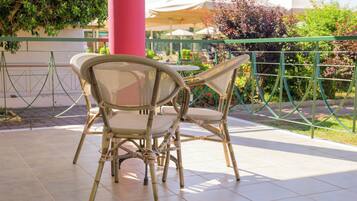 Un espace extérieur abrité, aménagé avec deux fauteuils en osier et une table, entouré d’une clôture verte et d’un pilier rouge.