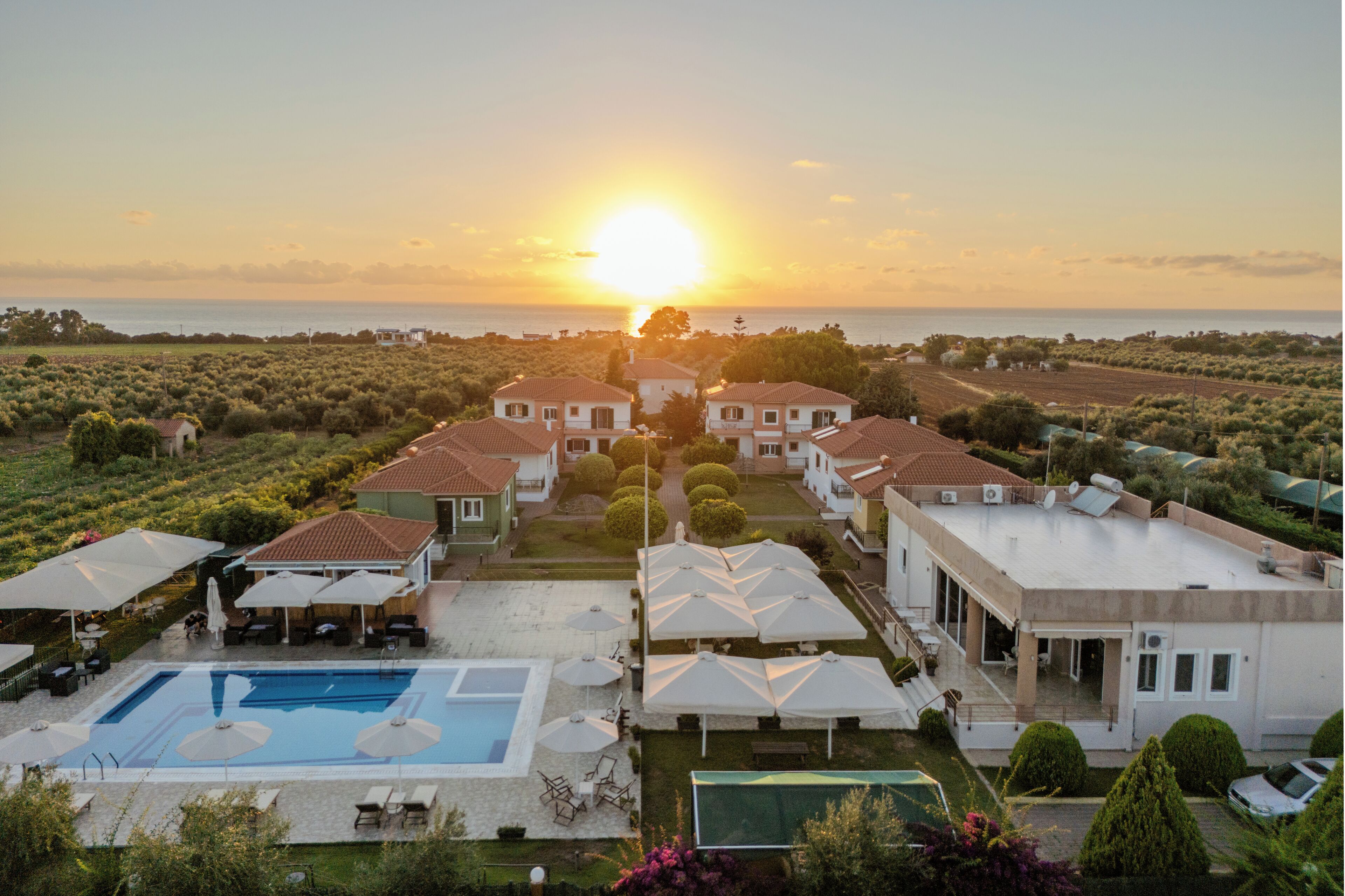 A resort with multiple villas, a swimming pool, and a view of the sea at sunset.