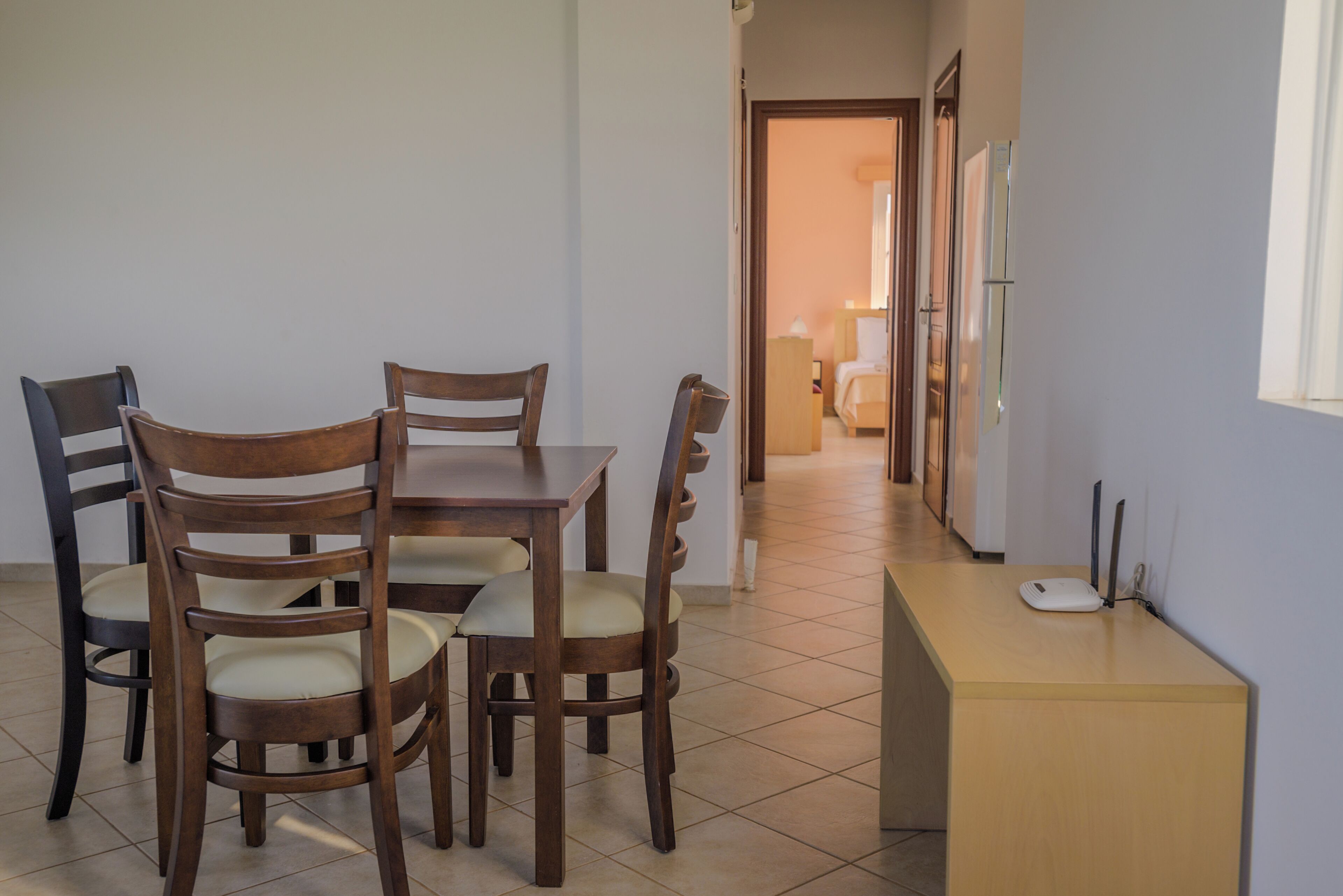 A dining area with a wooden table and chairs, a small kitchenette with a refrigerator, and a hallway leading to a bedroom.