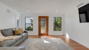 Un salón moderno con sofá de cuero, alfombra estampada y puerta de madera con panel de vidrio decorativo.