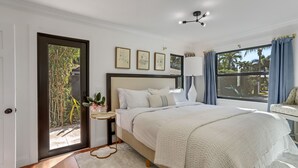 Un dormitorio con cama, mesita de noche, ventana con cortinas y puerta que da a un espacio exterior.