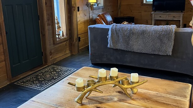 Et hyggeligt interiør i en hytte med trægulv, en sofa med et tæppe, et fjernsyn og en dekorativ lysestage på et bord.