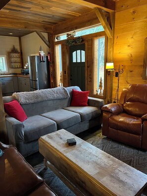 Un salón acogedor con un sofá gris, cojines rojos, un sillón de cuero marrón y una mesa de centro de madera.