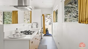 A narrow kitchen with a coffee station, a stove, and a view of a rocky landscape through large windows. - Stars on the Rocks: Pool/HotTub/FirePit/Boulders! (Joshua Tree)