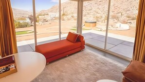A modern room with a red sofa, large windows, and a view of a desert landscape. - Stars on the Rocks: Pool/HotTub/FirePit/Boulders! (Joshua Tree)