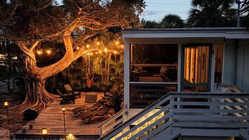 A wooden deck with a staircase leading to a building, surrounded by trees and string lights.