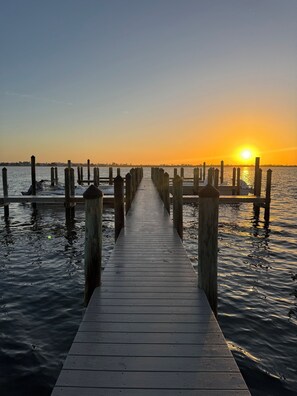 Une jetée en bois s’étendant sur une étendue d’eau calme, avec un coucher de soleil en arrière-plan.