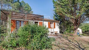 Une maison rustique, dotée d’un toit de chaume, entourée d’une végétation luxuriante et d’arbres.
