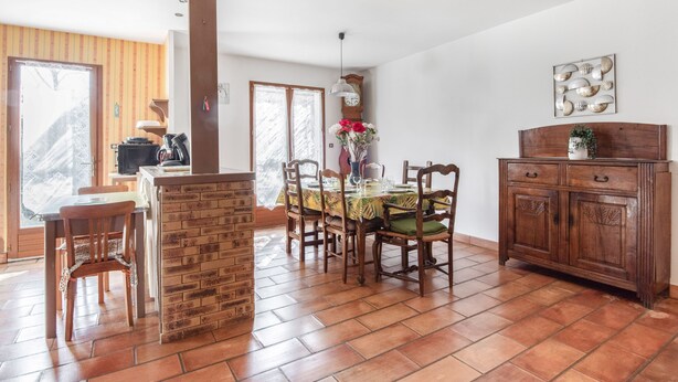 Un espace repas agrémenté d’un mur en briques, de chaises en bois, d’une table ornée d’un centre de table floral et d’un buffet en bois doté de tiroirs.