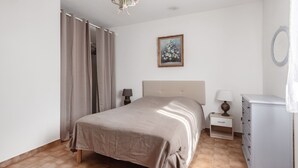 Une chambre à coucher comprenant un lit, des tables de chevet, une commode, un tableau et un lustre.