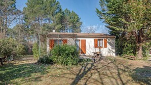 Une maison de campagne au toit de tuiles, entourée d’arbres touffus et d’une cour verdoyante.