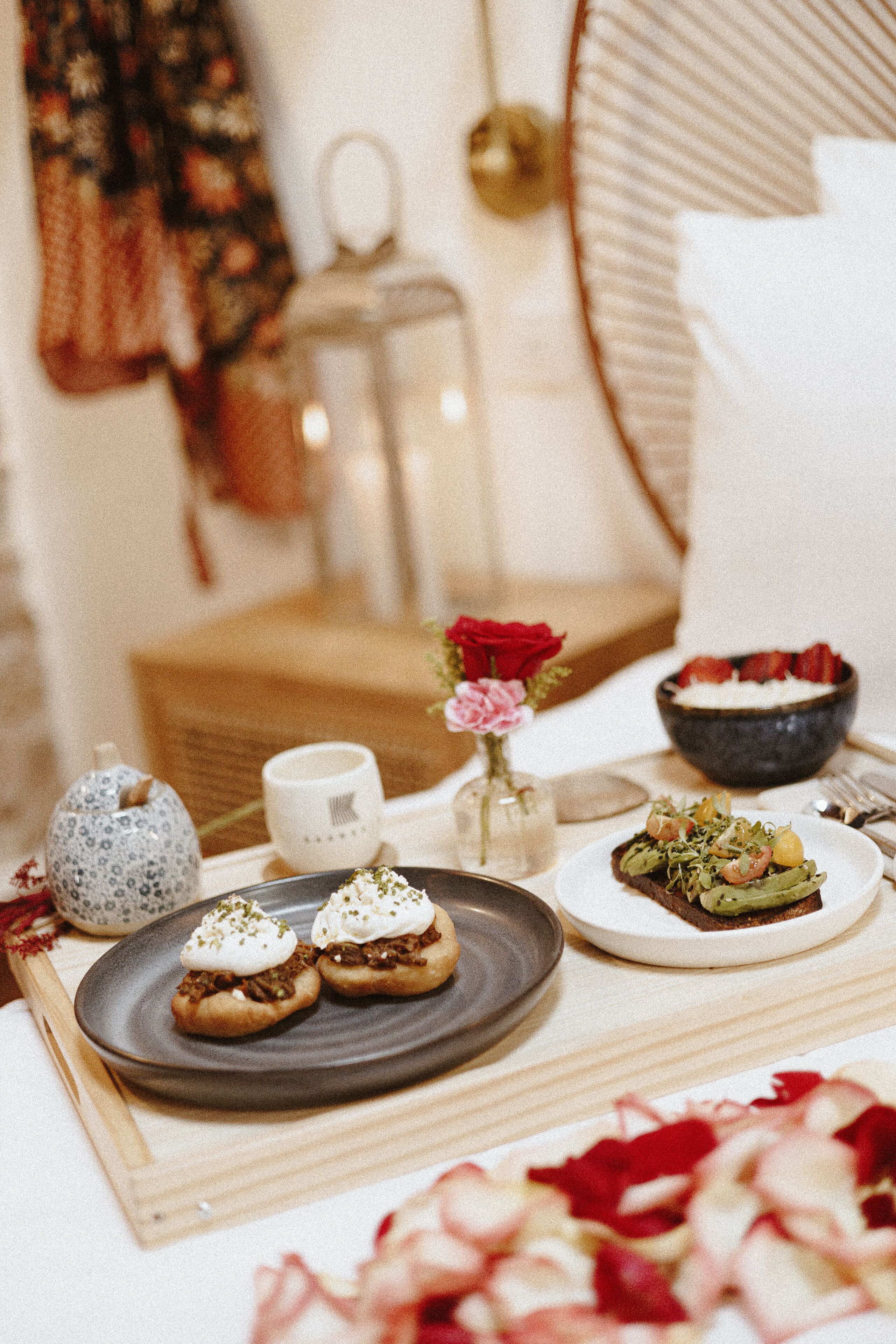 Une table à manger avec des assiettes remplies de nourriture, un vase contenant une rose rouge et une théière.