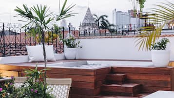 Terraço no telhado com piso xadrez, assentos de madeira, plantas em vasos e vista para a cidade.