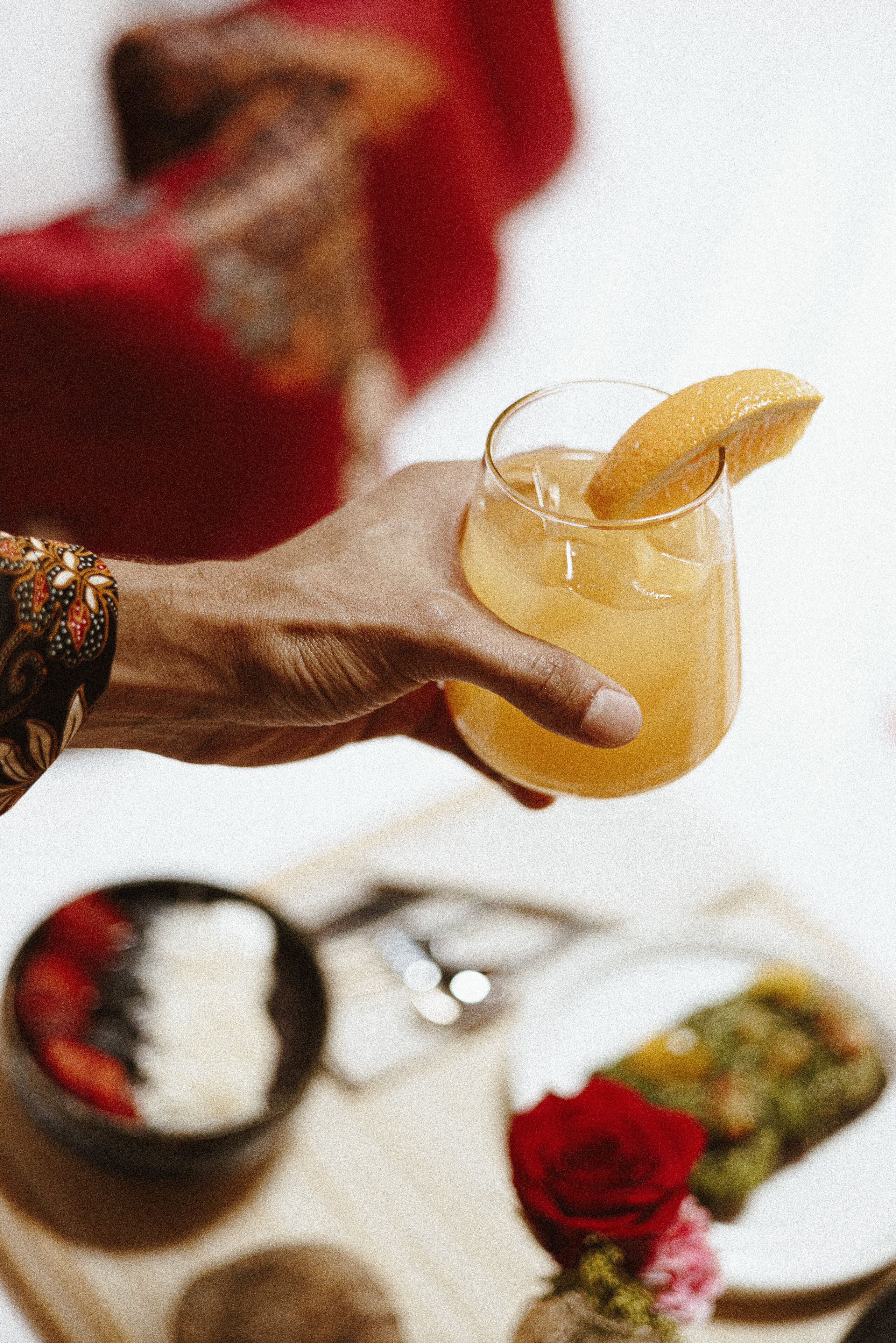 A hand holding a glass with a lemon slice garnish.