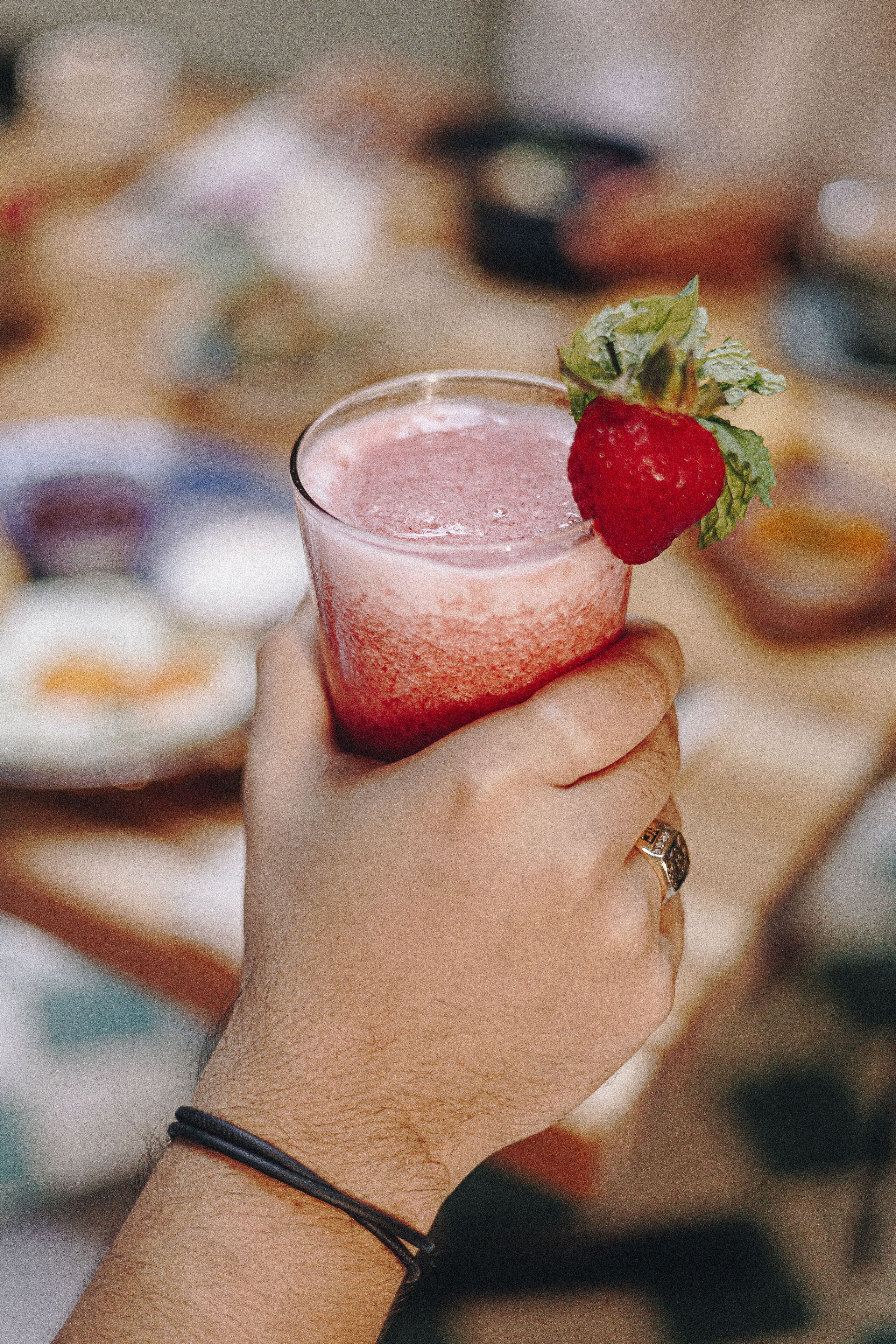 A hand holding a glass with a strawberry garnish.