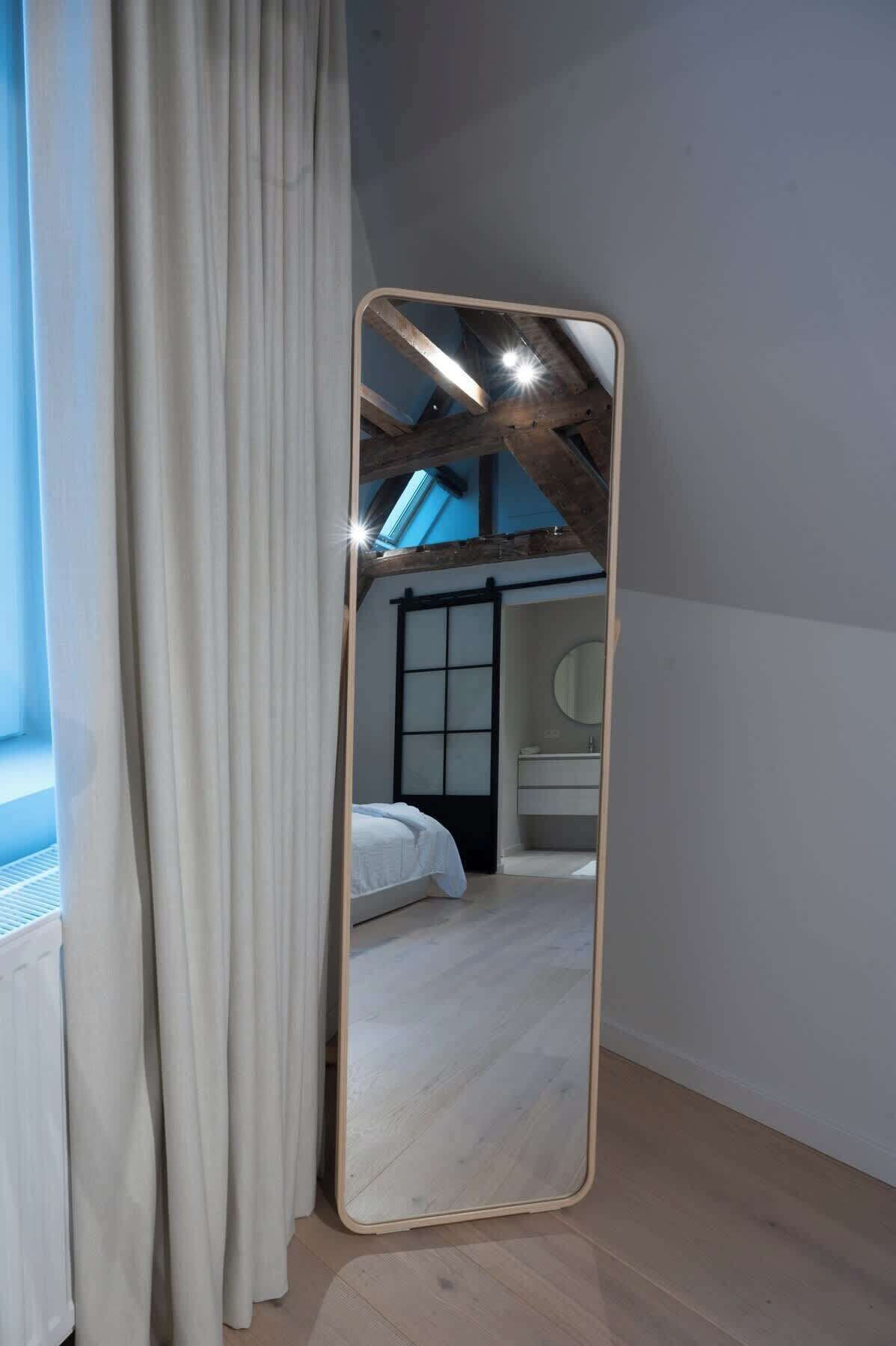 Un dormitorio con un espejo grande, vigas de madera, una cama y una ventana con cortinas.
