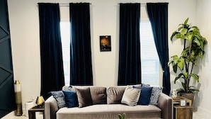 Ein modernes Wohnzimmer mit einem grauen Sofa, zwei Sesseln, einem Holztisch und einer großen Topfpflanze.