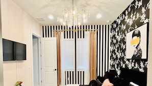 Ein modernes Schlafzimmer mit einem Bett, einem Fernseher, einer Kristallleuchtre und einem floralen Wanddekor.