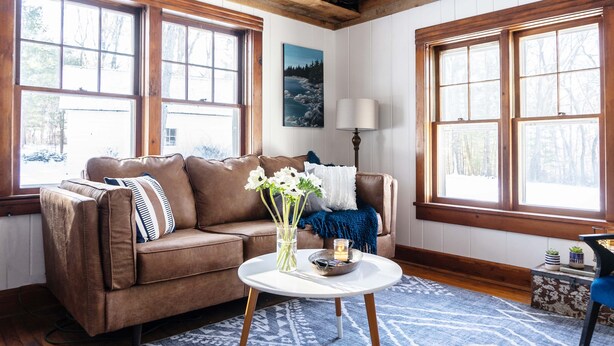 A cozy living room with a brown leather sofa, a white round coffee table, and a blue patterned rug. - Whimsical Woodland Cottage in Stone Ridge NY (Stone Ridge)