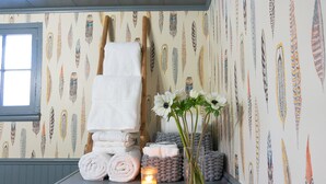 A neatly arranged bathroom with towels stacked, a vase with flowers, and a lit candle on a shelf. - Whimsical Woodland Cottage in Stone Ridge NY (Stone Ridge)