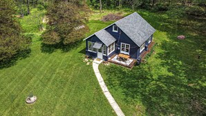 A two-story house with a dark blue exterior, a front porch with a table and chairs, and a visible pathway leading to the entrance. - Whimsical Woodland Cottage in Stone Ridge NY (Stone Ridge)