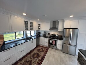 A modern kitchen with white cabinets, stainless steel appliances, and a large window offering a view of the outdoors.