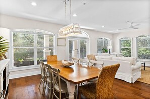 Relax in a spacious living area with a large dining table and comfortable seating near large windows offering a view of the surrounding greenery.