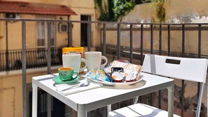 Un balcon avec une table préparée pour le petit-déjeuner, comprenant une tasse verte, une tasse blanche, une assiette avec de la nourriture et une boisson.
