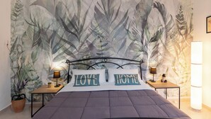 Une chambre avec un grand lit, deux tables de chevet avec des lampes et une fresque murale représentant des feuilles.