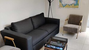 A living room with a black sofa, a grey armchair, a glass coffee table, and a map on the wall.