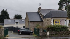 A residential area with a black car parked in front of a stone building with a sign that reads "SCOOT."