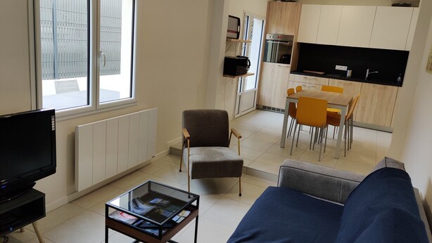 A modern living room with a sofa, a glass coffee table, a TV, and a dining area with a table and chairs.
