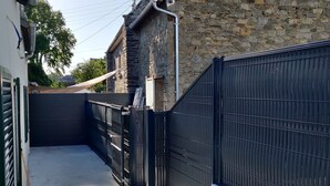 A narrow alleyway with a black metal fence, a concrete floor, and a wooden bench.
