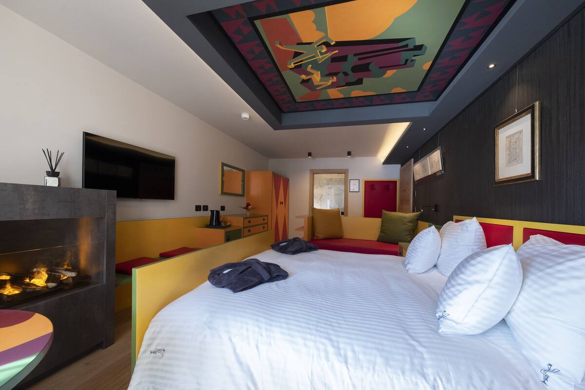 A modern hotel room with a large bed, a fireplace, a television, and artwork on the walls.