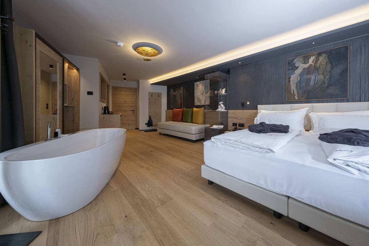 A modern bedroom with a large white bathtub, a bed with white linens, and a wooden floor.