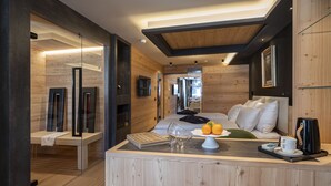 A modern bedroom with a wooden ceiling, a bed with white bedding, a bedside table with a coffee maker, and a view into the adjacent room. - Art Hotel Locanda degli Artisti (Canazei)