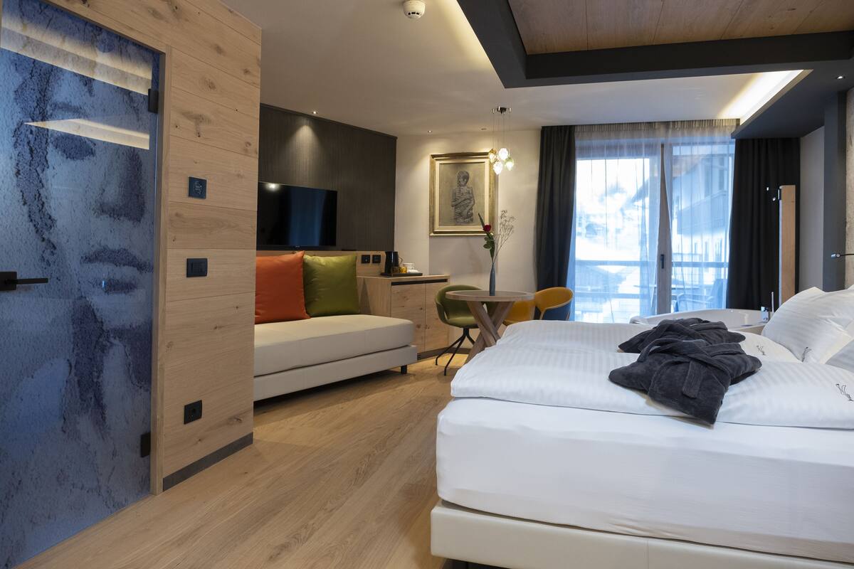 A modern hotel room with a bed, a sofa, a desk, and a television.
