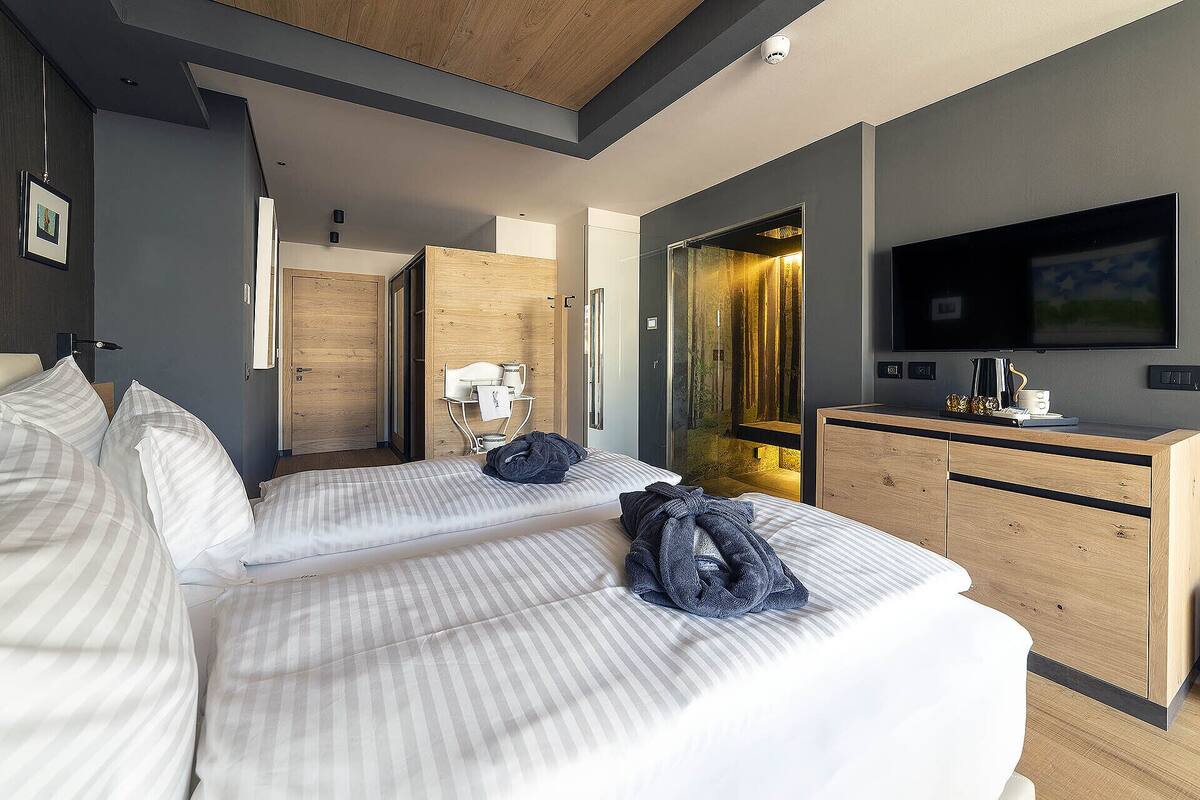 A hotel room with two beds, a TV, a desk, and a shower area.