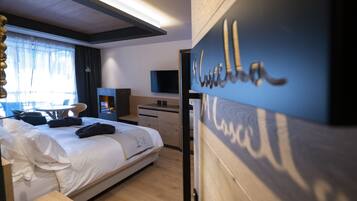 A hotel room with a bed, a desk, a chair, a TV, and a wooden wall with the name 'M. Louise'.