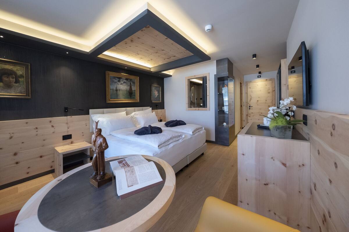 A modern hotel room with a large bed, bedside tables, a round table with a statue, and a mirror.